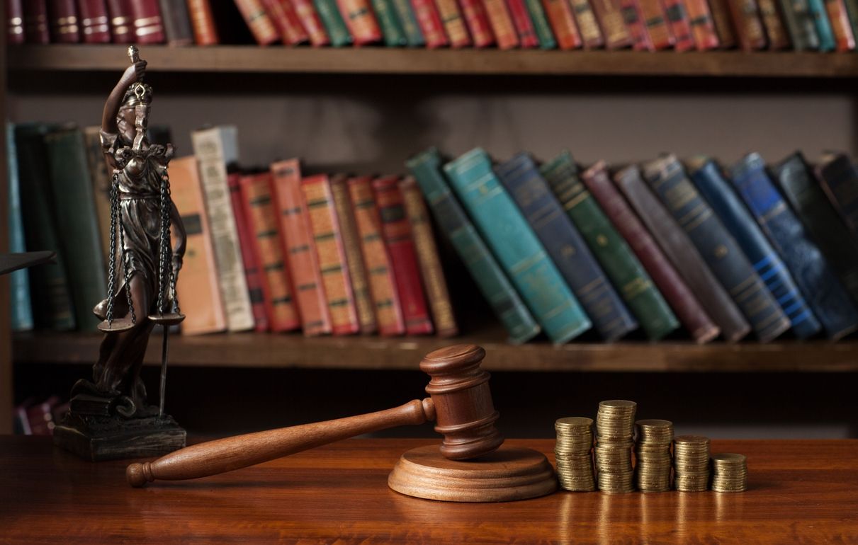 Bücherregal vor dem Justitia, ein Hammer und gestapelte Münzen stehen